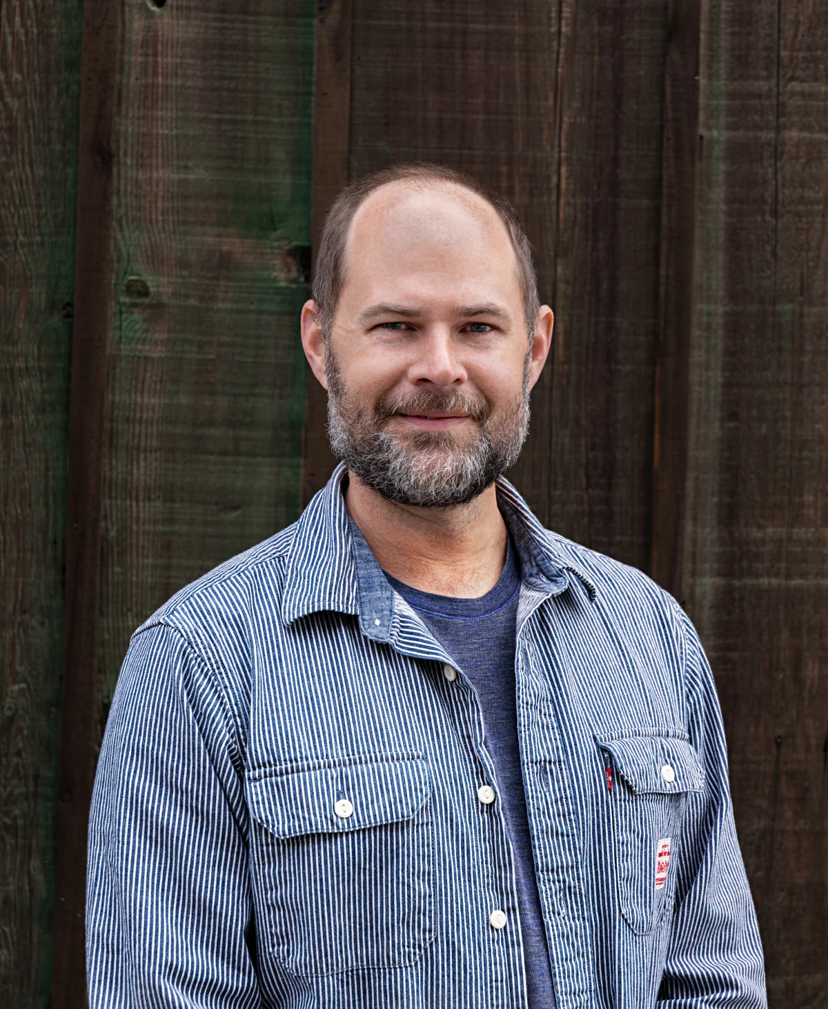 Adam Taplin in a striped shirt against a wood wall