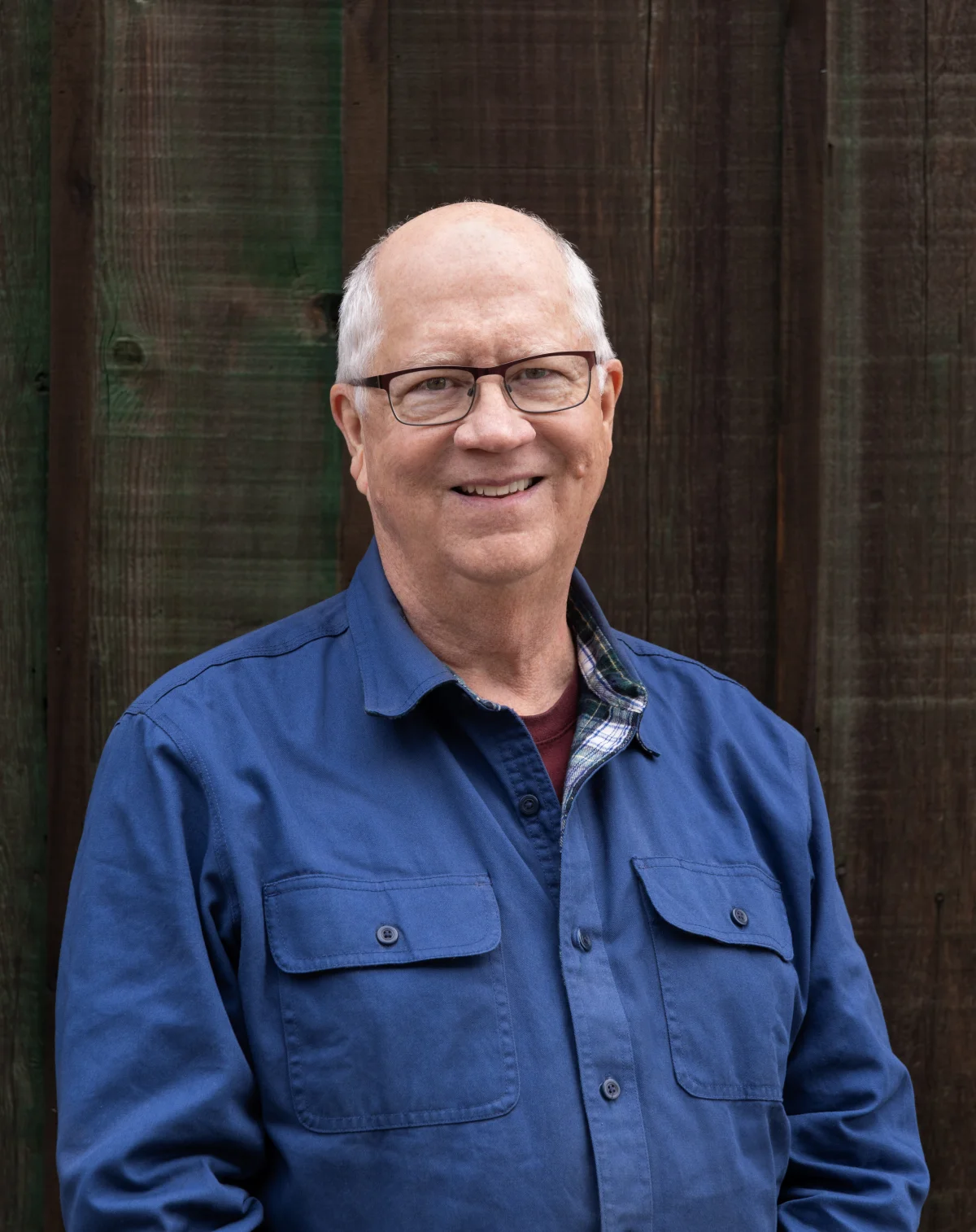 Bill Taplin smiling in a blue work shirt against a wood wall